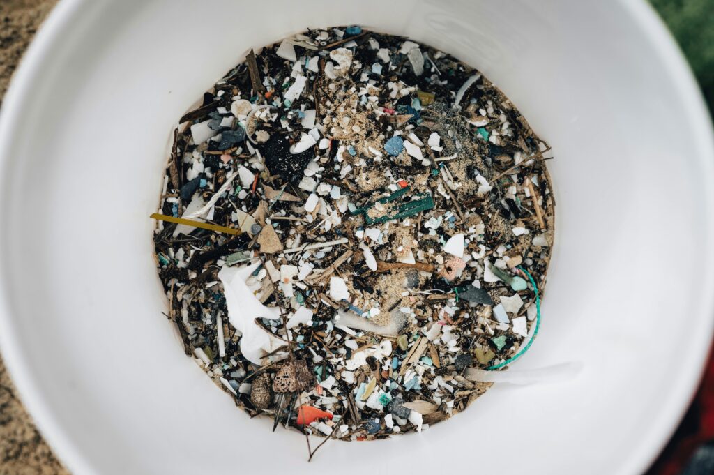 Detailed view of microplastics and debris collected in a white circular container showing pollution.
