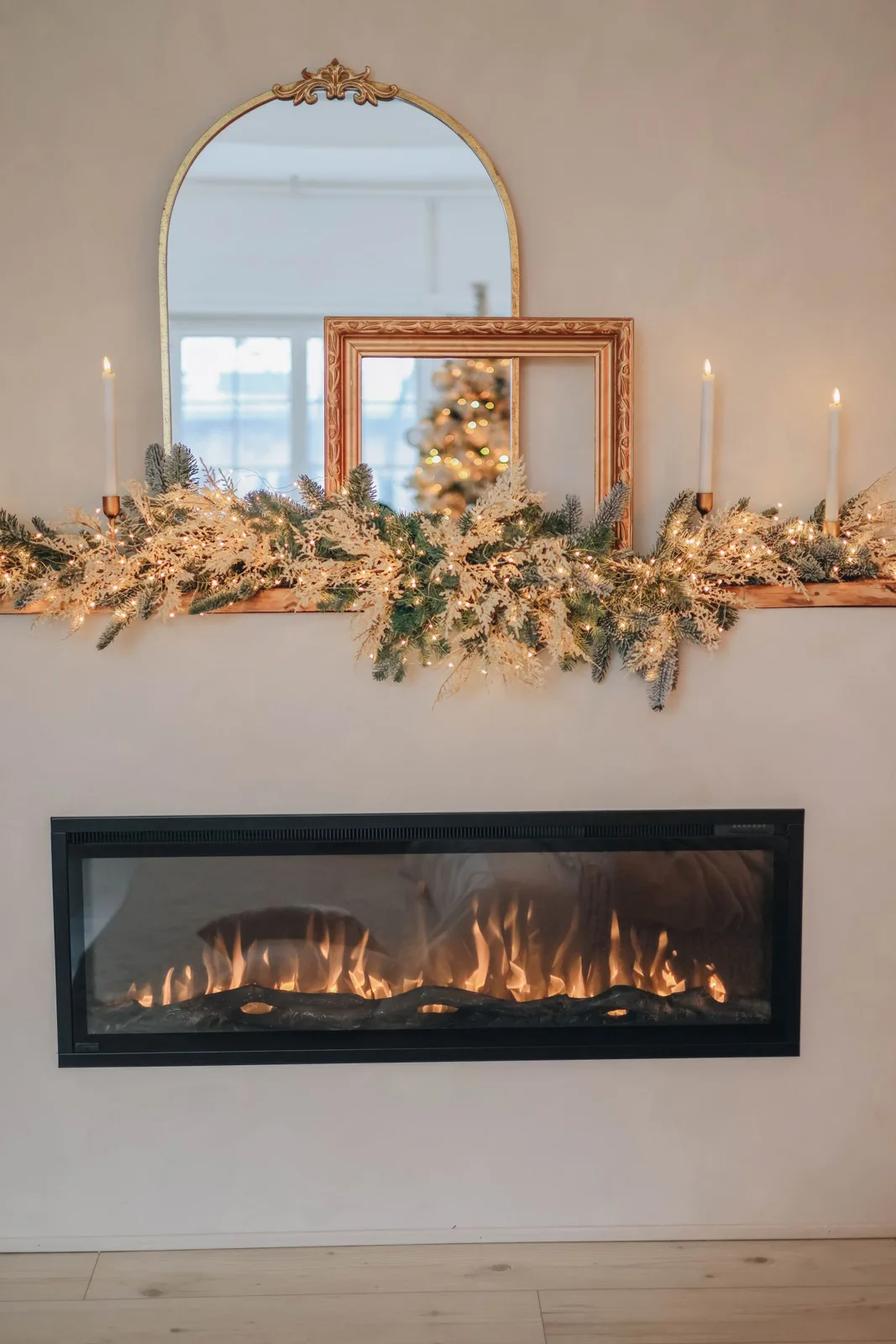Lit candles and Christmas greenery arranged on a decorated fireplace mantel