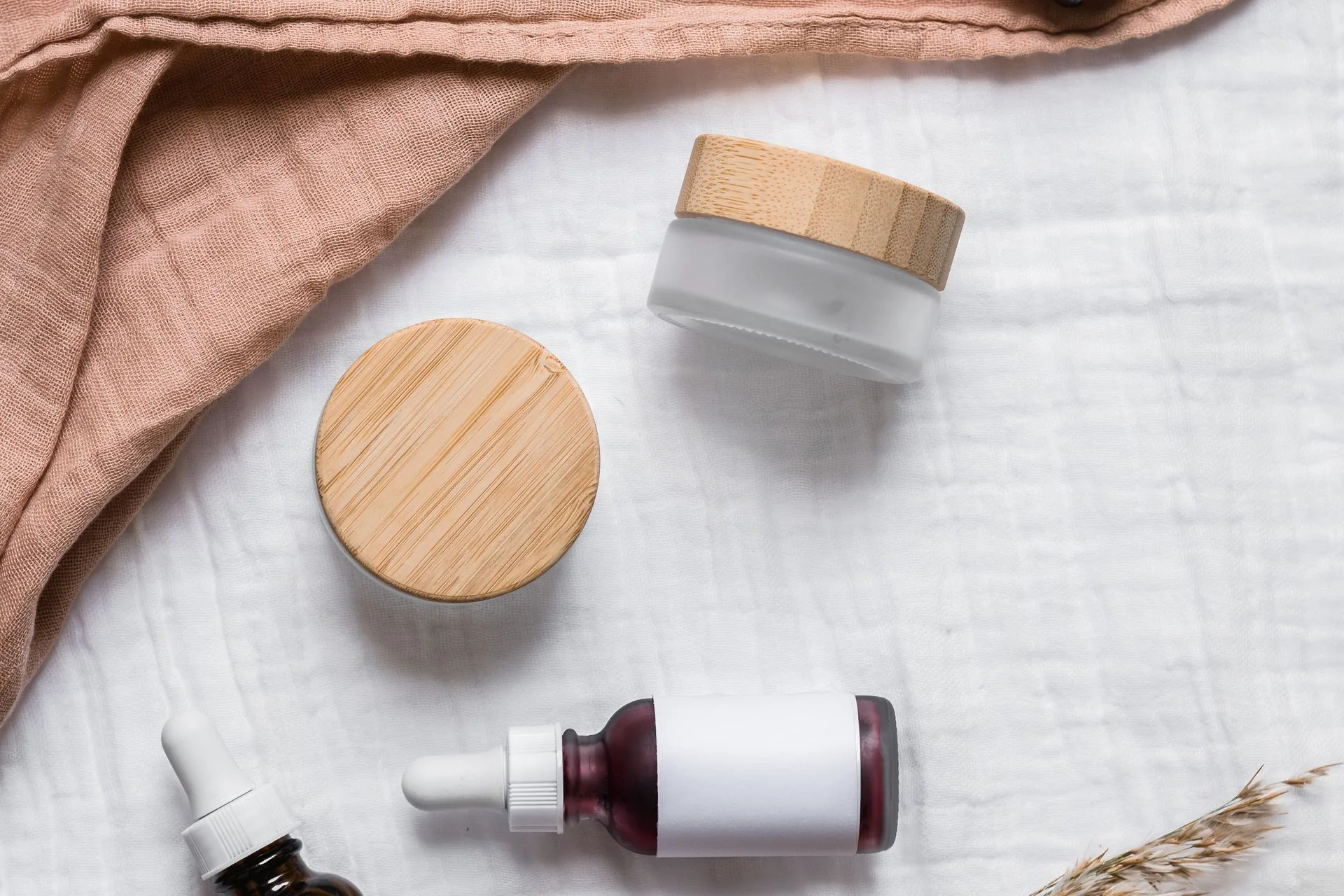 Natural beauty gifts for her on cream linen: solid shampoo bars, a glass bottle of face oil, a metal safety razor, glass nail polish bottles and a folded merino sweater
