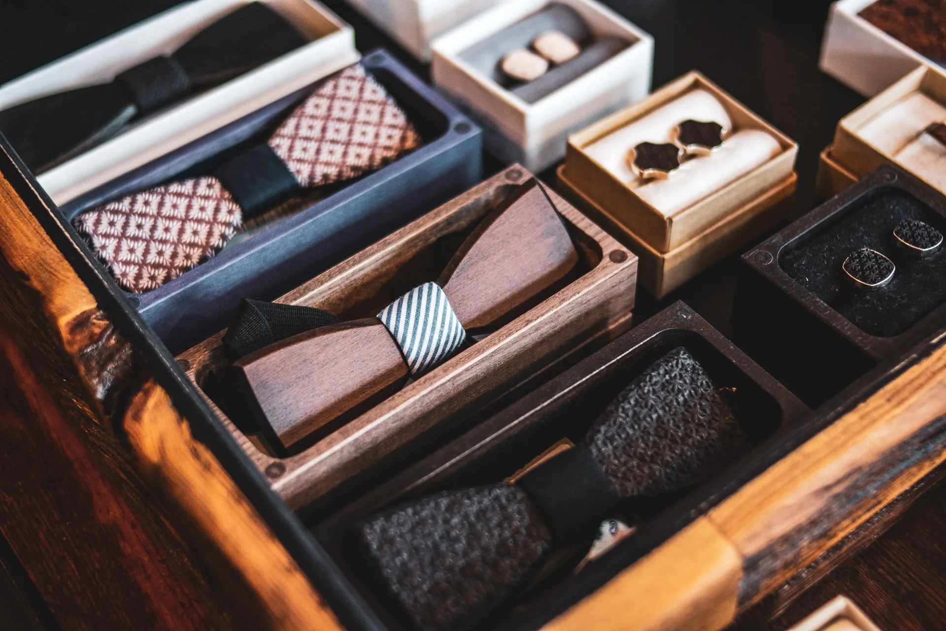 Christmas gifts for him: a waxed canvas jacket on a hook, folded flannel and merino layers, a safety razor and a stainless steel bottle on a wooden bench