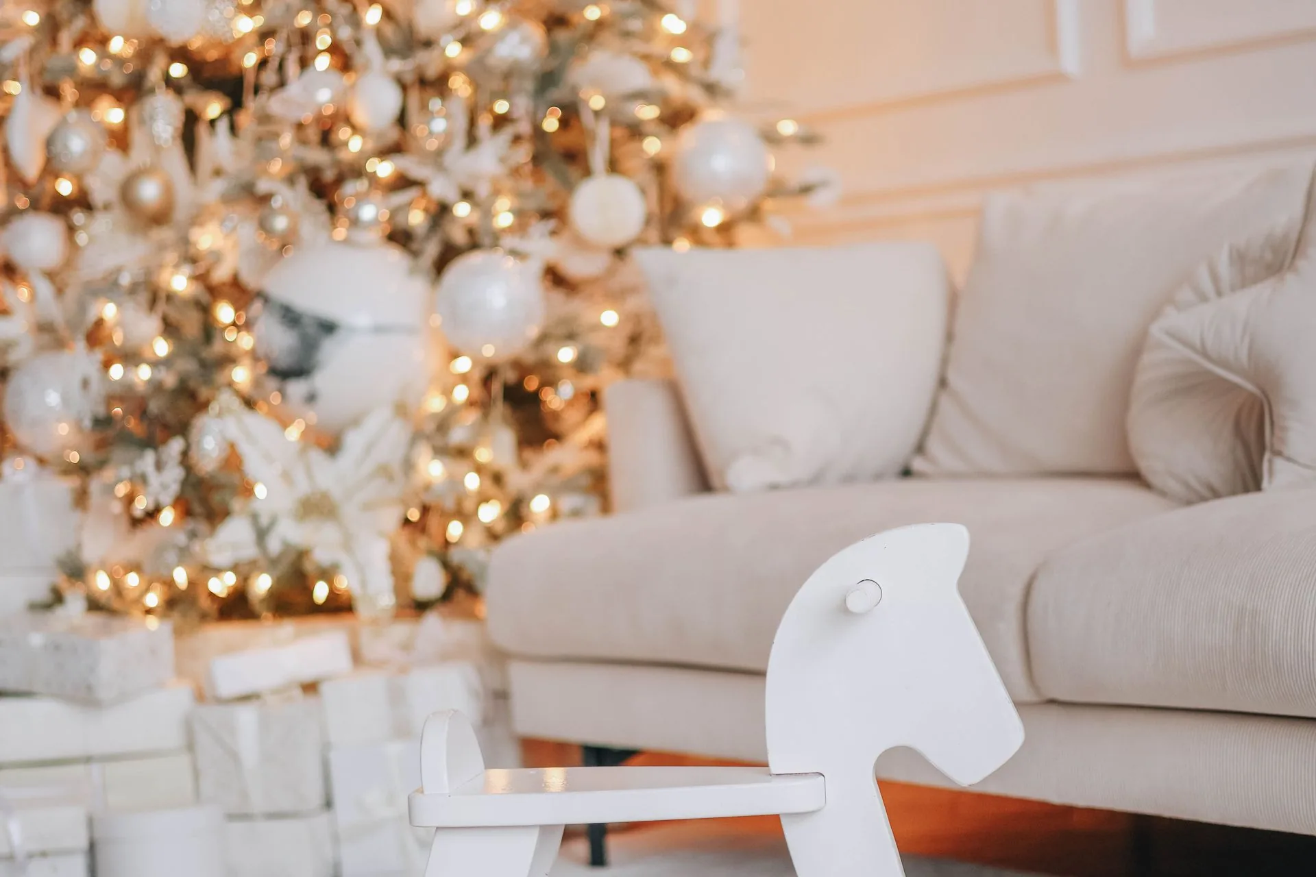 Wooden Christmas toys for kids: building blocks, a wooden train, a dollhouse and a silk playsilk beside a small Christmas tree