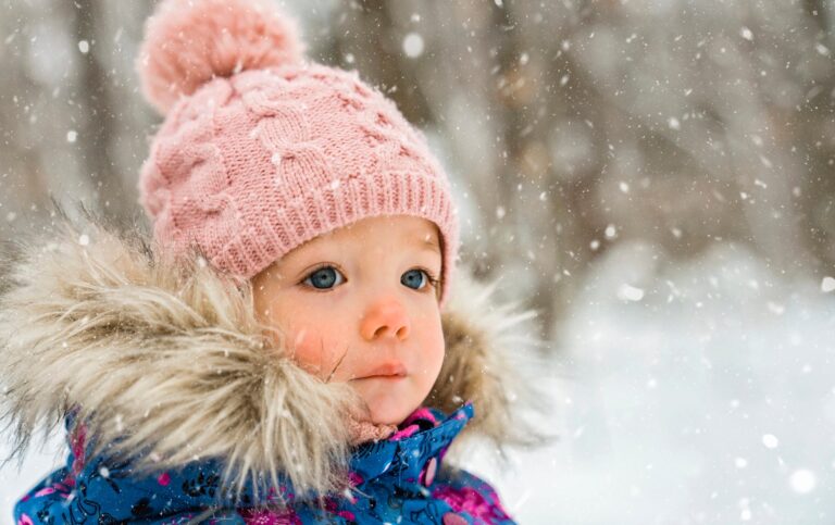 Young child wearing a winter coat with a fur-trimmed hood in falling snow