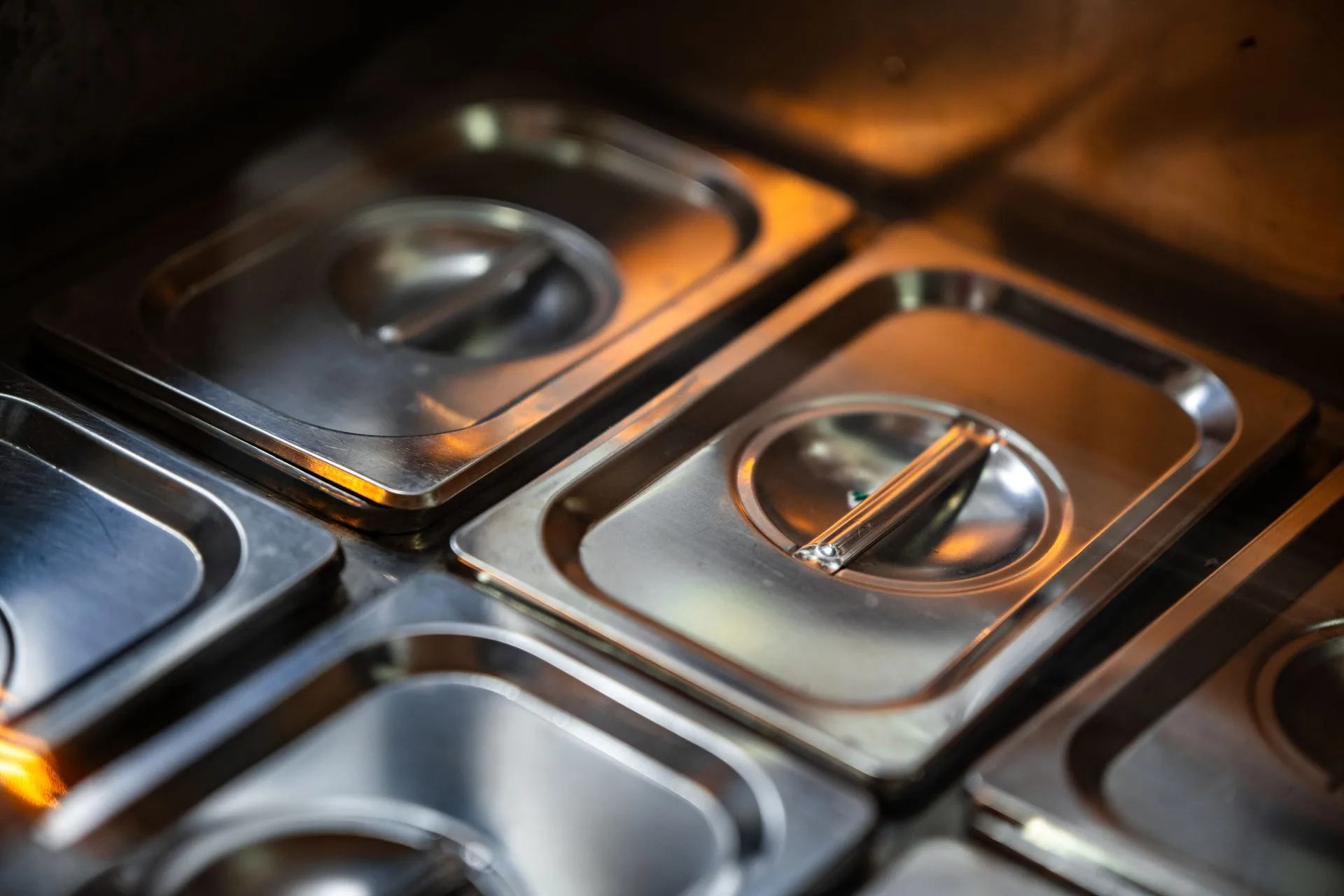 Stacked stainless steel food containers with lids in warm kitchen light
