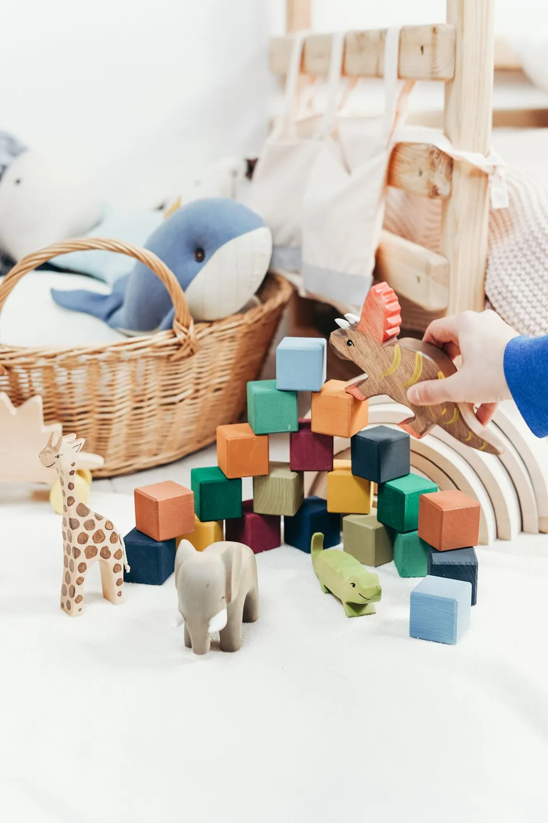 A child's hand playing with colorful wooden blocks and carved wooden animal figures on a playroom floor