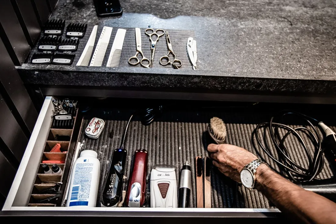 A barber's drawer of grooming tools: scissors, combs, a straight razor and clippers laid out on a counter